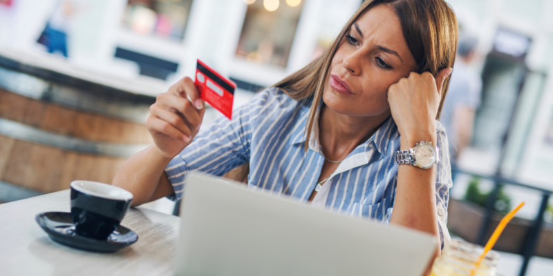 Woman looking worried and confused as she contemplates a credit card in front of her laptop.