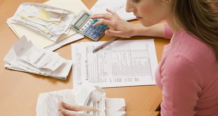 woman at a desk doing her taxes, surrounded by receipts, forms, and a calculator