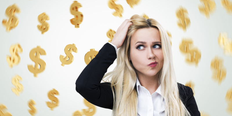 Portrait of a confused blond businesswoman scratching her head while standing near a gray wall with dollar signs