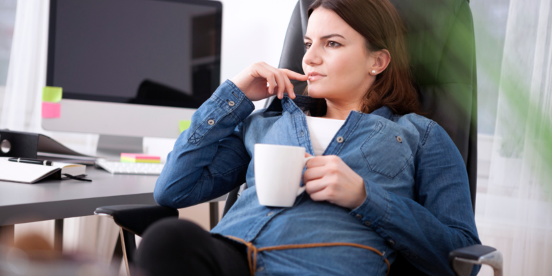 Businesswoman sitting pondering relaxing over a mug of coffee at her desk staring into the distance with a contemplative expression