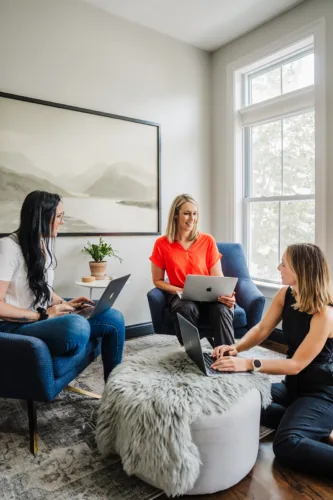 Nicki Krawczyk and members of the Fired Up Freelance team sit in a living room with laptops and work in a circle