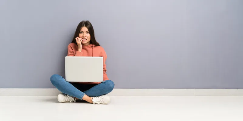 Woman sitting on the floor with a laptop with a nervous look